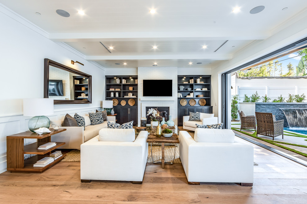 Photo of a transitional open concept living room in Los Angeles with white walls, light hardwood floors, a standard fireplace, a wall-mounted tv and beige floor.
