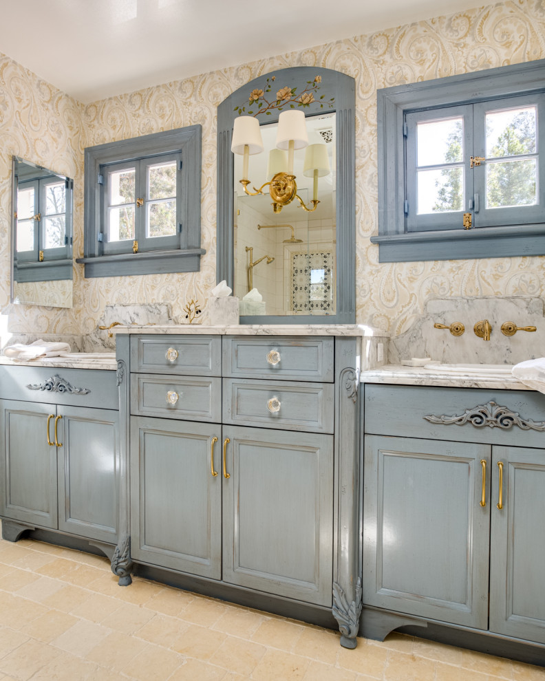 Идея дизайна: большая главная ванная комната в классическом стиле с синими фасадами, тумбой под две раковины, встроенной тумбой, обоями на стенах, фасадами с утопленной филенкой, угловым душем, мраморной плиткой, желтыми стенами, полом из известняка, накладной раковиной, мраморной столешницей, бежевым полом и белой столешницей