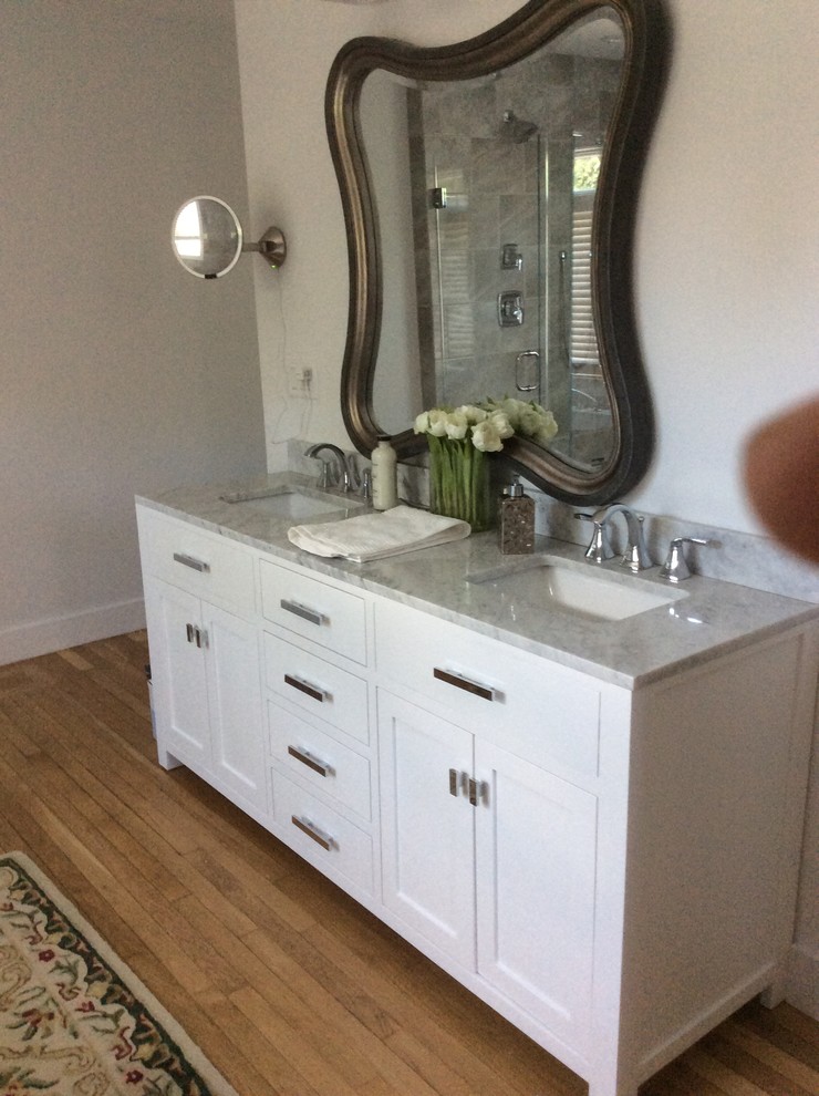 This is an example of a mid-sized traditional 3/4 bathroom in Boston with recessed-panel cabinets, white cabinets, a freestanding tub, a corner shower, ceramic tile, grey walls, light hardwood floors, an undermount sink and marble benchtops.