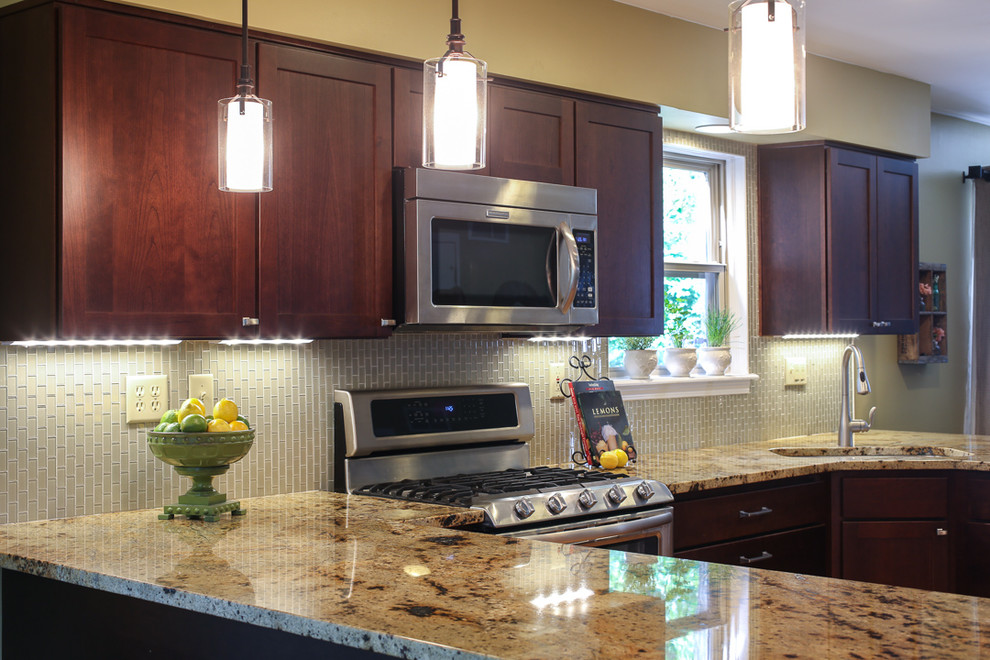 Example of a transitional medium tone wood floor kitchen design with an undermount sink, shaker cabinets, dark wood cabinets, granite countertops, white backsplash, glass tile backsplash and stainless steel appliances