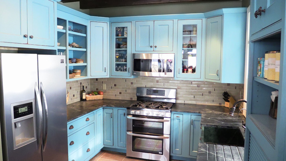 Photo of a mid-sized beach style u-shaped separate kitchen in Baltimore with a farmhouse sink, recessed-panel cabinets, blue cabinets, soapstone benchtops, grey splashback, ceramic splashback, stainless steel appliances, porcelain floors and a peninsula.