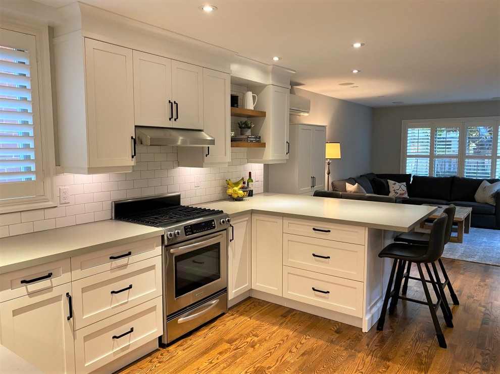Mid-sized transitional u-shaped medium tone wood floor and brown floor open concept kitchen photo in Toronto with an undermount sink, shaker cabinets, white cabinets, quartz countertops, white backsplash, porcelain backsplash, stainless steel appliances, a peninsula and gray countertops