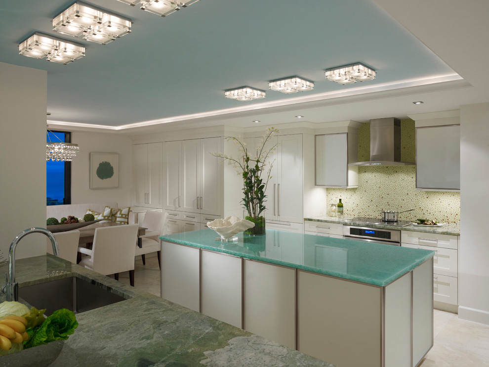 This is an example of a beach style eat-in kitchen in Miami with an undermount sink, shaker cabinets, white cabinets, mosaic tile splashback and stainless steel appliances.