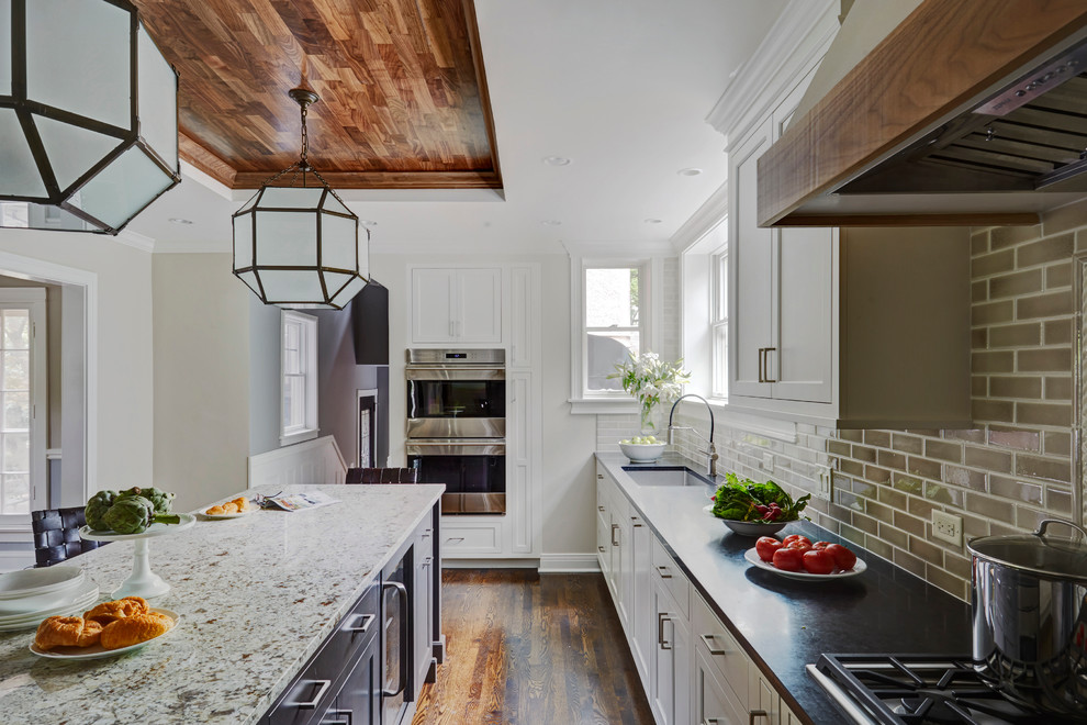 Design ideas for a mid-sized transitional l-shaped separate kitchen in Chicago with recessed-panel cabinets, white cabinets, beige splashback, with island, granite benchtops, an undermount sink, subway tile splashback, stainless steel appliances and dark hardwood floors.