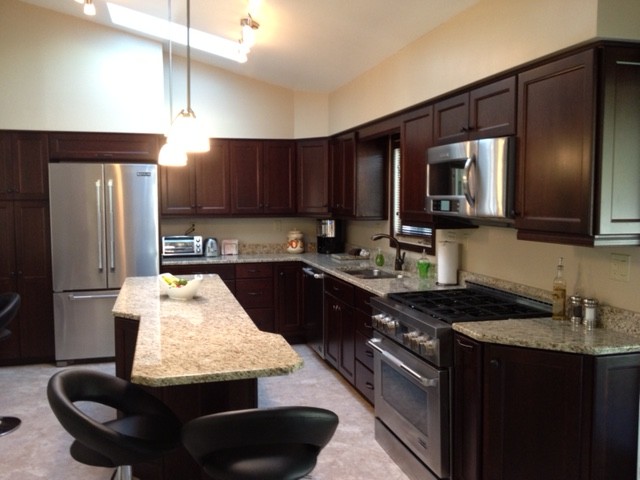 Eat-in kitchen - transitional porcelain tile eat-in kitchen idea with a double-bowl sink, recessed-panel cabinets, brown cabinets, granite countertops, beige backsplash, stone slab backsplash, stainless steel appliances and an island