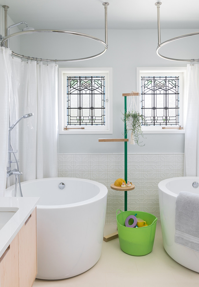 This is an example of a scandinavian kids bathroom in Seattle with flat-panel cabinets, light wood cabinets, a japanese tub, a shower/bathtub combo, white tile, ceramic tile, porcelain floors, an undermount sink, solid surface benchtops, a shower curtain, white benchtops, grey walls and beige floor.