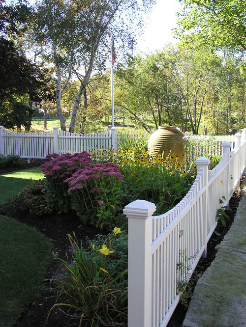 A lovely picket fence surrounding a colorful garden filled with black eyed susans and other types of daisies. A lovely way to add curb appeal.