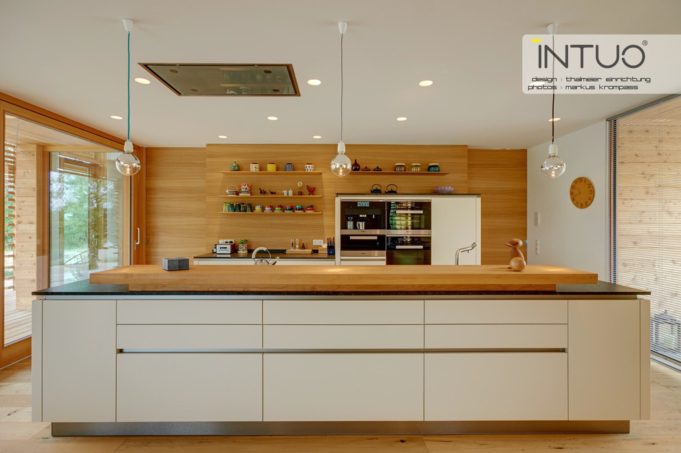This is an example of an expansive scandi single-wall open plan kitchen in Other with a submerged sink, flat-panel cabinets, white cabinets, granite worktops, black appliances, light hardwood flooring and an island.
