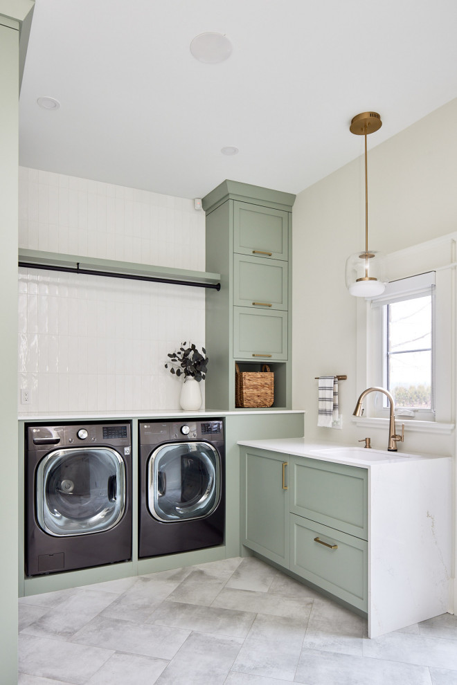 Example of a mid-sized transitional porcelain tile and gray floor laundry room design with an undermount sink, green cabinets, quartz countertops, white backsplash, ceramic backsplash, beige walls, a side-by-side washer/dryer and white countertops