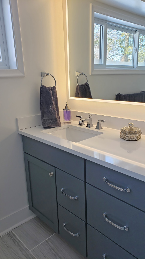 Walk-in shower - large transitional master gray tile and porcelain tile porcelain tile, gray floor and double-sink walk-in shower idea with shaker cabinets, gray cabinets, a two-piece toilet, white walls, an undermount sink, quartz countertops, a hinged shower door, white countertops, a niche and a built-in vanity