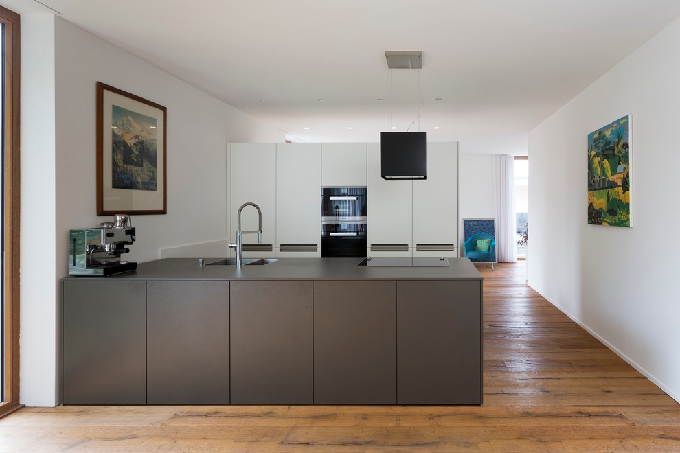 This is an example of a mid-sized contemporary open plan kitchen in Frankfurt with flat-panel cabinets, white cabinets, medium hardwood floors, wood benchtops, black appliances and a peninsula.