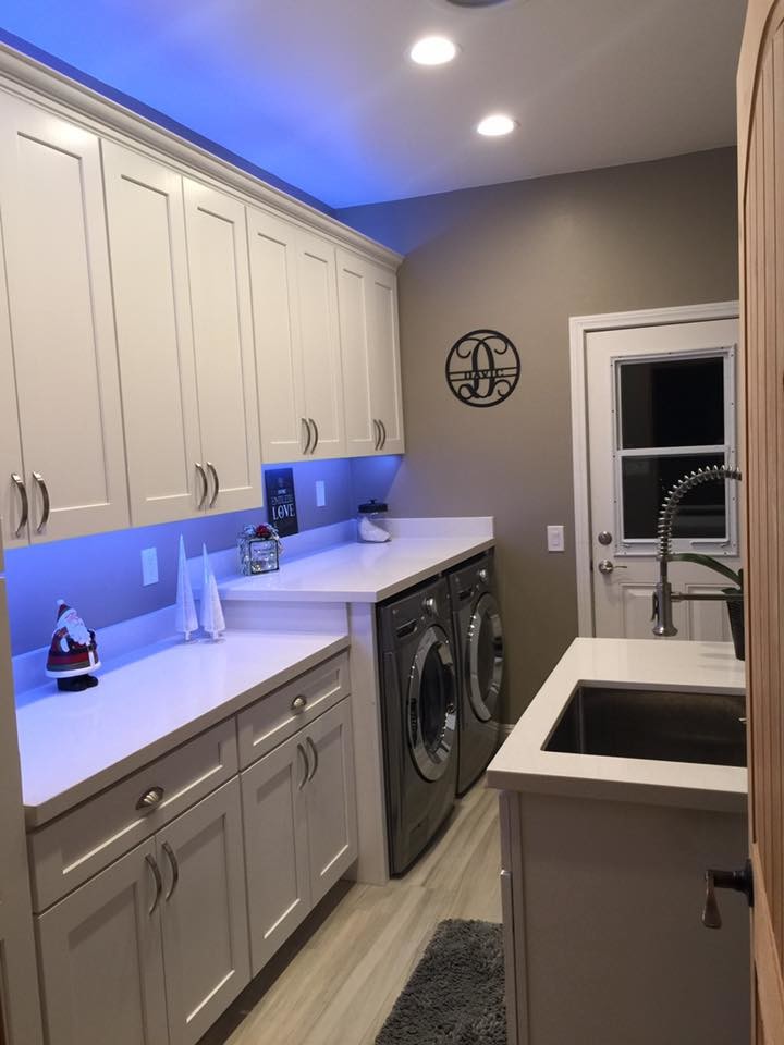 Photo of a mid-sized contemporary single-wall dedicated laundry room in San Diego with an undermount sink, recessed-panel cabinets, white cabinets, solid surface benchtops, beige walls, porcelain floors, a side-by-side washer and dryer and beige floor.