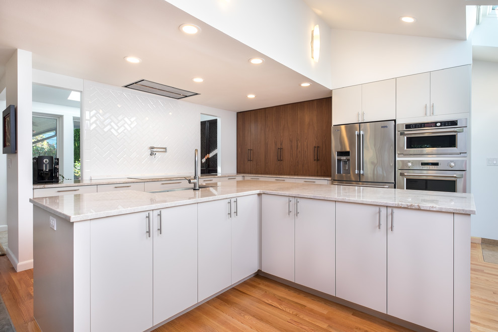 Inspiration for a large transitional l-shaped medium tone wood floor open concept kitchen remodel in Portland with an undermount sink, flat-panel cabinets, white cabinets, quartzite countertops, white backsplash, ceramic backsplash, stainless steel appliances and an island