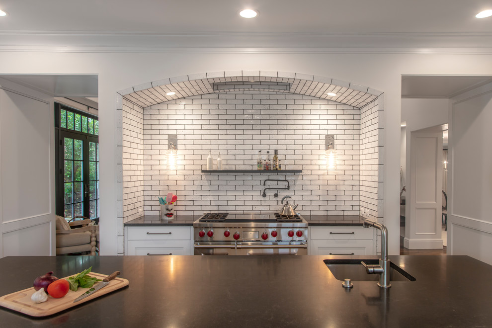 Expansive transitional u-shaped eat-in kitchen in Detroit with white splashback, subway tile splashback, stainless steel appliances, a farmhouse sink, shaker cabinets, white cabinets, concrete benchtops, dark hardwood floors, with island, brown floor and black benchtop.
