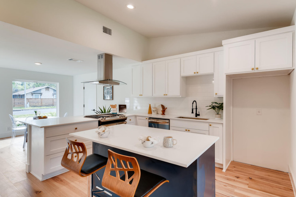 Photo of a mid-sized modern l-shaped eat-in kitchen in Denver with a drop-in sink, shaker cabinets, white cabinets, quartzite benchtops, white splashback, marble splashback, stainless steel appliances, light hardwood floors, with island and white benchtop.