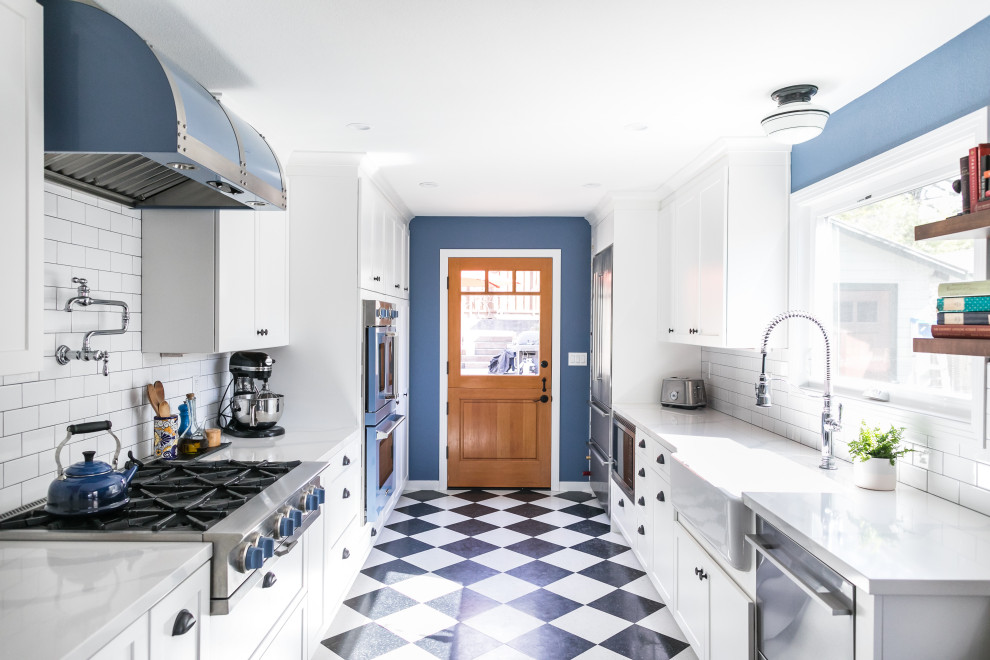 Photo of a mid-sized eclectic galley eat-in kitchen in San Francisco with a farmhouse sink, shaker cabinets, white cabinets, quartz benchtops, white splashback, ceramic splashback, coloured appliances, vinyl floors, no island, black floor and white benchtop.