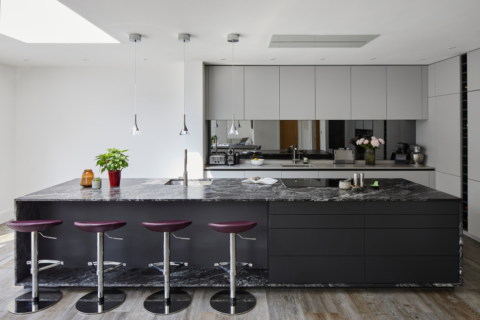Inspiration for a large contemporary l-shaped eat-in kitchen in Kent with flat-panel cabinets, grey cabinets, granite benchtops, mirror splashback, stainless steel appliances, with island and black benchtop.