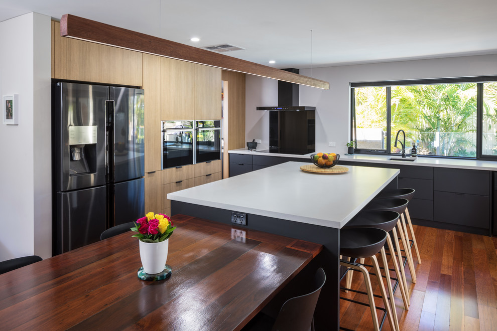 Inspiration for a contemporary l-shaped eat-in kitchen in Perth with flat-panel cabinets, light wood cabinets, quartz benchtops, black splashback, glass sheet splashback, black appliances, with island, grey benchtop, an undermount sink, medium hardwood floors and brown floor.