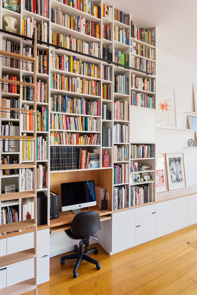 Ispirazione per un piccolo studio minimal con libreria, pareti bianche, scrivania incassata, pavimento in legno massello medio e pavimento marrone