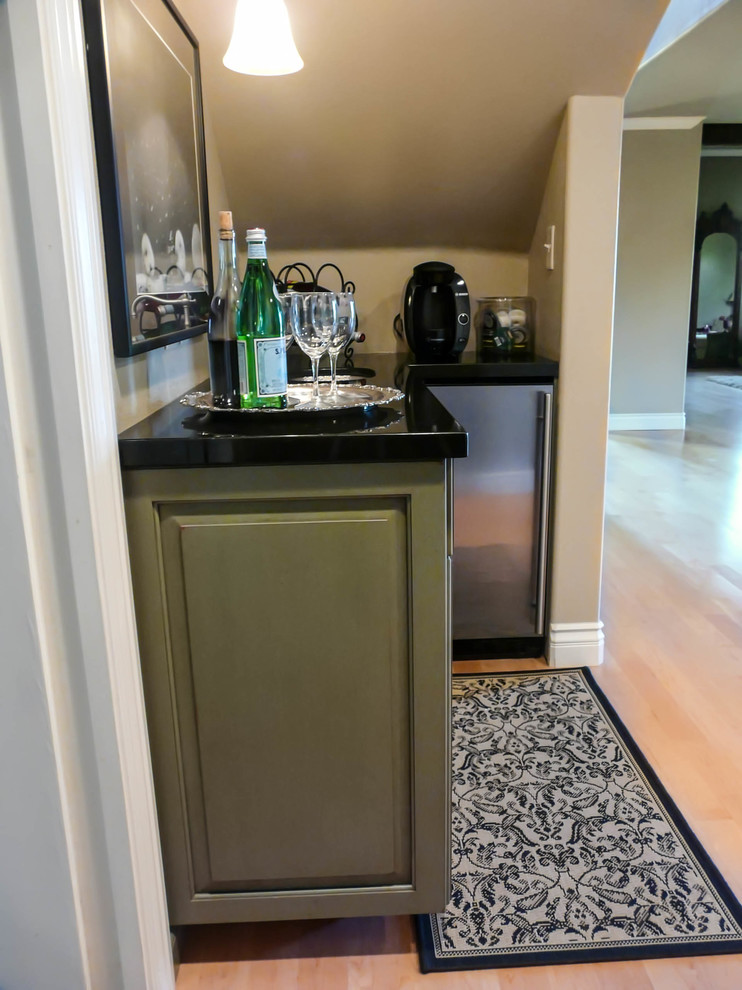 Photo of a small transitional l-shaped wet bar in San Diego with an undermount sink, raised-panel cabinets, green cabinets, granite benchtops and light hardwood floors.
