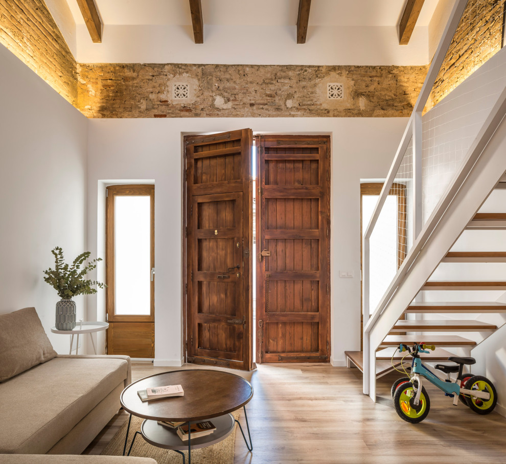 Пример оригинального дизайна: маленькая открытая гостиная комната в средиземноморском стиле с разноцветными стенами, полом из ламината, коричневым полом, балками на потолке и кирпичными стенами без телевизора для на участке и в саду