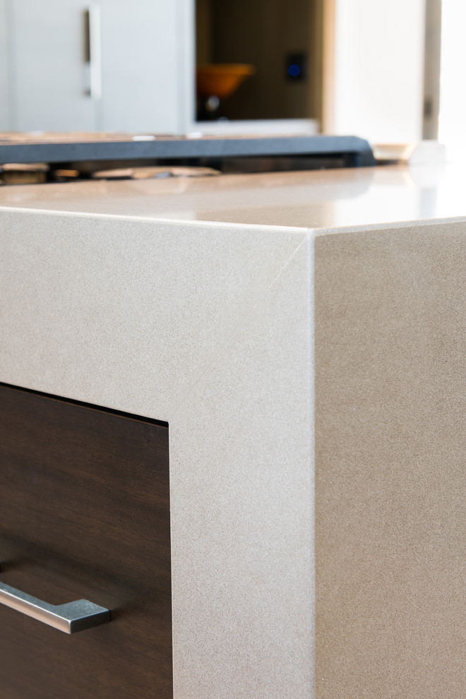 Example of a transitional kitchen design with quartz countertops, an island, flat-panel cabinets and brown cabinets
