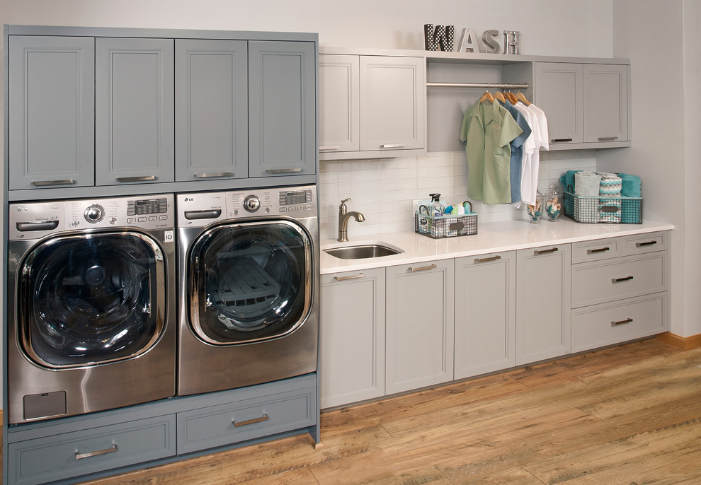Design ideas for a mid-sized traditional single-wall dedicated laundry room in Seattle with an undermount sink, recessed-panel cabinets, grey cabinets, solid surface benchtops, grey walls, dark hardwood floors, a side-by-side washer and dryer and brown floor.