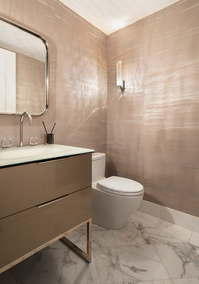 Small trendy marble floor and white floor bathroom photo in New York with flat-panel cabinets, a one-piece toilet, an integrated sink, glass countertops and brown walls