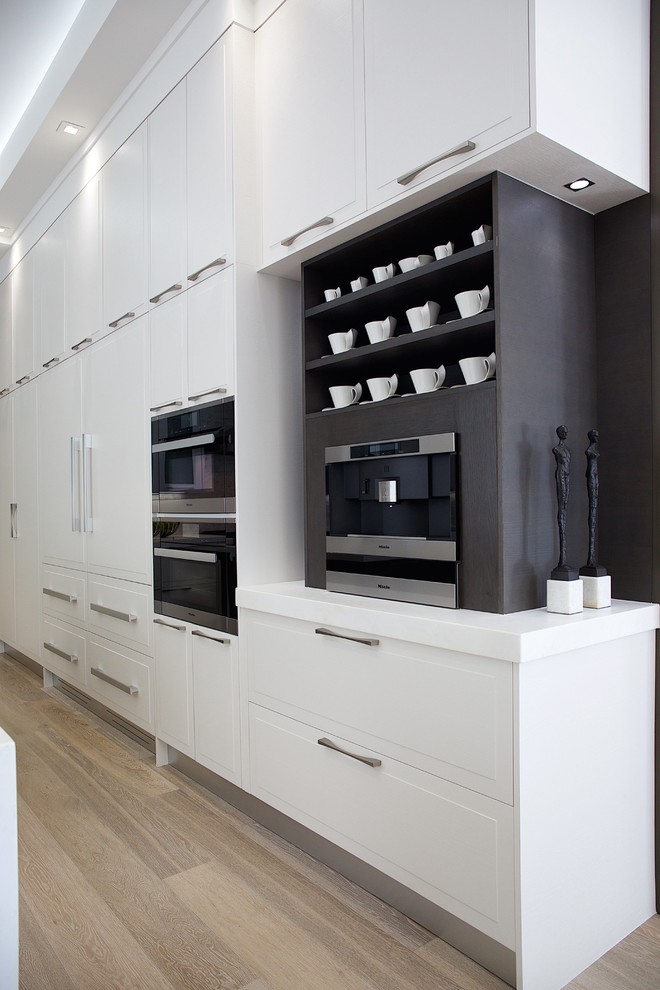 Photo of a large contemporary u-shaped eat-in kitchen in Miami with a single-bowl sink, glass-front cabinets, white cabinets, solid surface benchtops, grey splashback, stone tile splashback, panelled appliances, ceramic floors and multiple islands.