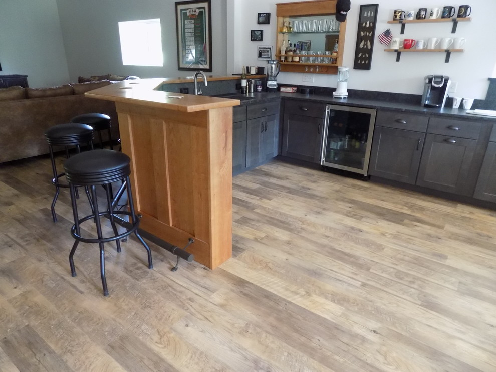 Photo of a large industrial u-shaped seated home bar in Boston with an undermount sink, shaker cabinets, dark wood cabinets, wood benchtops, black splashback, stone slab splashback, vinyl floors, brown floor and brown benchtop.