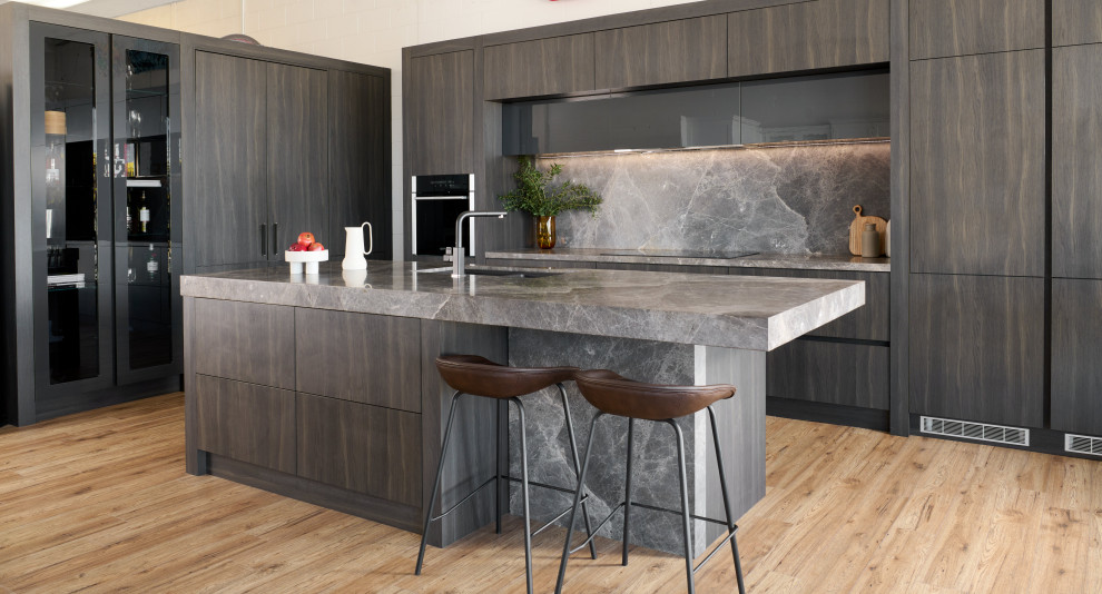 Inspiration for a contemporary l-shaped kitchen with a submerged sink, flat-panel cabinets, dark wood cabinets, black appliances, light hardwood flooring, an island, beige floors and grey worktops.