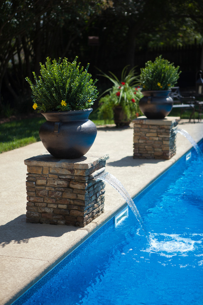 Photo of a mid-sized traditional backyard custom-shaped pool in Charlotte with a water feature and concrete slab.