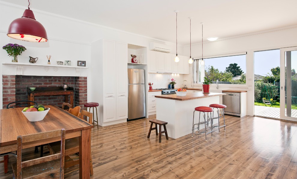 This is an example of a mid-sized contemporary l-shaped kitchen in Melbourne with a farmhouse sink, raised-panel cabinets, white cabinets, wood benchtops, white splashback, stainless steel appliances and with island.
