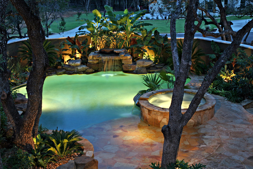 Design ideas for a mid-sized tropical backyard custom-shaped natural pool in Austin with natural stone pavers and a hot tub.