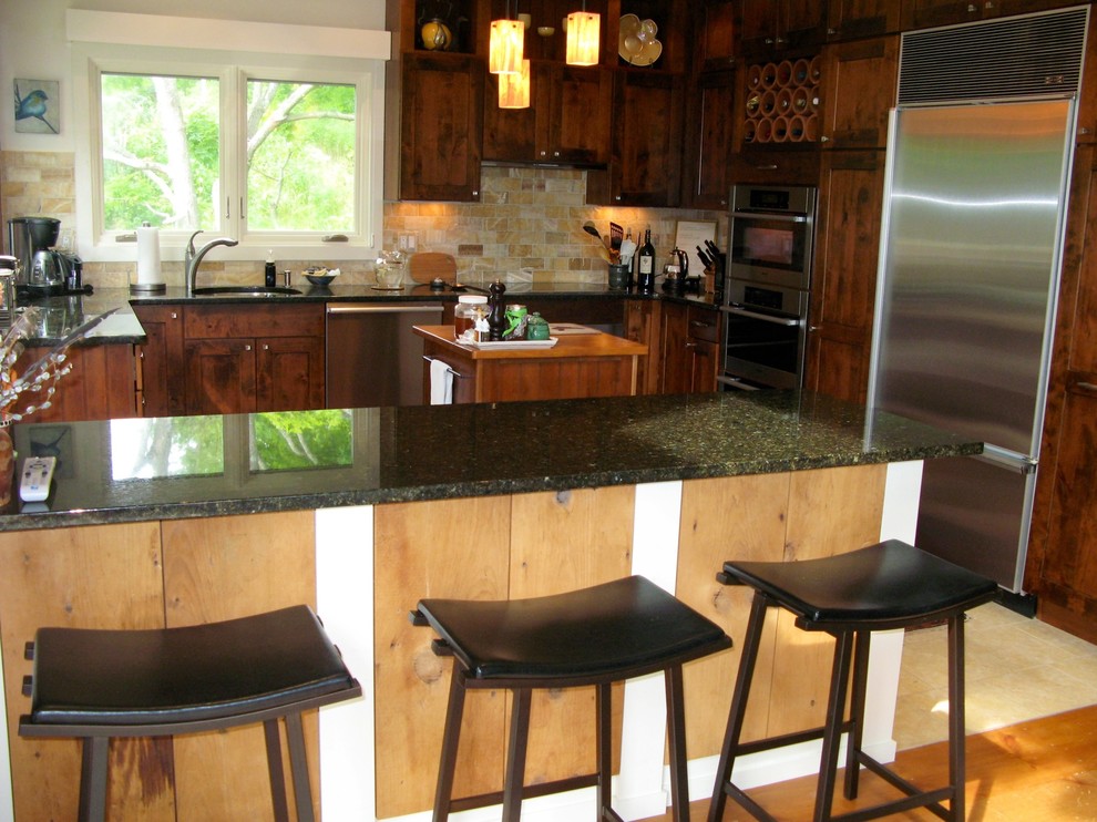 This is an example of a mid-sized country u-shaped eat-in kitchen in Other with an undermount sink, shaker cabinets, medium wood cabinets, granite benchtops, beige splashback, stone tile splashback, stainless steel appliances, limestone floors, with island, beige floor, black benchtop and exposed beam.