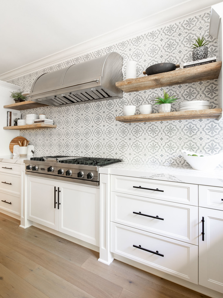Inspiration for a transitional kitchen in Orange County with a farmhouse sink, quartz benchtops, cement tile splashback, stainless steel appliances, light hardwood floors, with island and white benchtop.