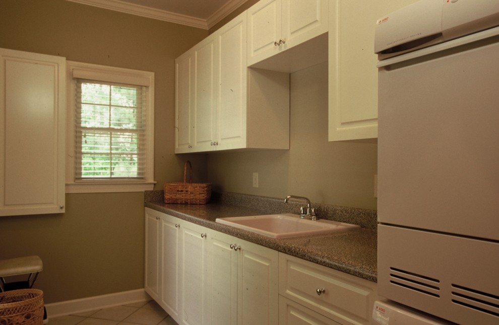 Large traditional single-wall utility room in Atlanta with a drop-in sink, raised-panel cabinets, white cabinets, laminate benchtops, beige walls, ceramic floors and a stacked washer and dryer.