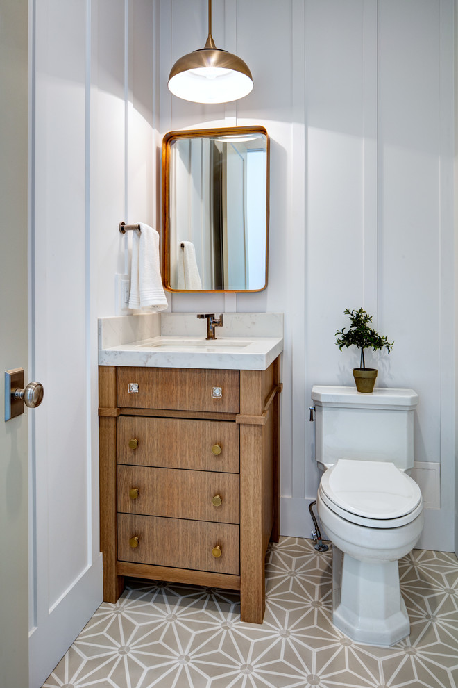 Small beach style powder room in Salt Lake City with furniture-like cabinets, a one-piece toilet, an undermount sink, marble benchtops, medium wood cabinets, white walls, beige floor and white benchtops.