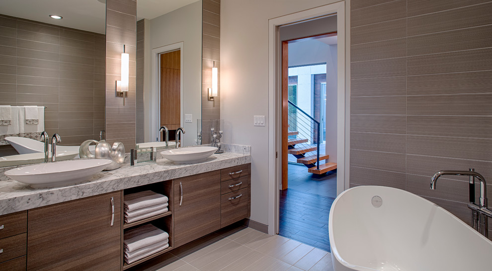 Mid-sized modern master bathroom in Houston with a vessel sink, flat-panel cabinets, medium wood cabinets, marble benchtops, a freestanding tub, an open shower, a two-piece toilet, gray tile, porcelain tile, white walls and porcelain floors.