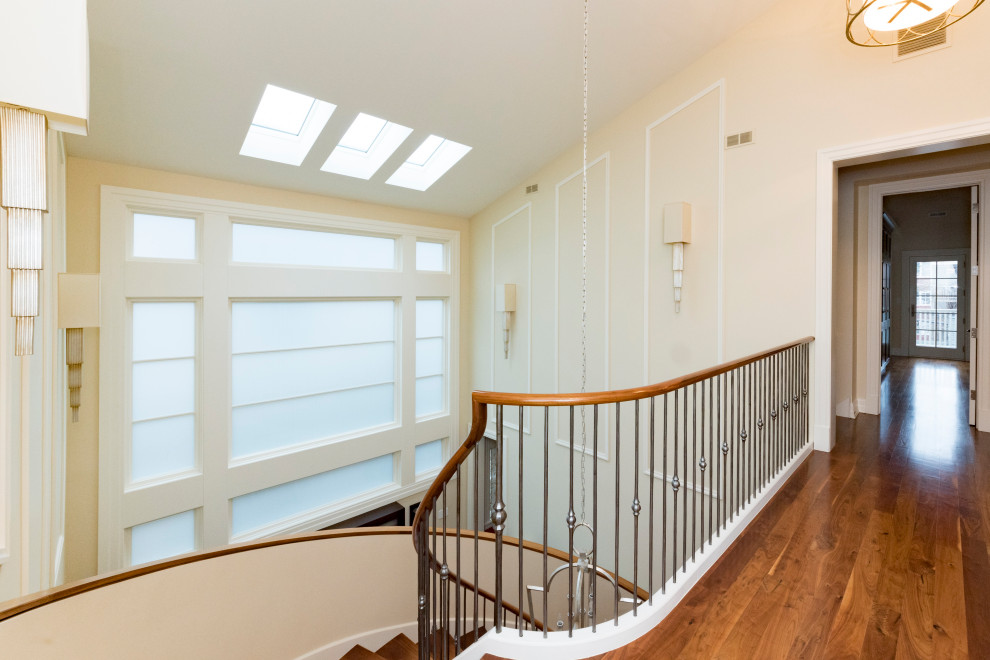 Example of a large transitional wooden curved metal railing and wainscoting staircase design in Chicago with painted risers
