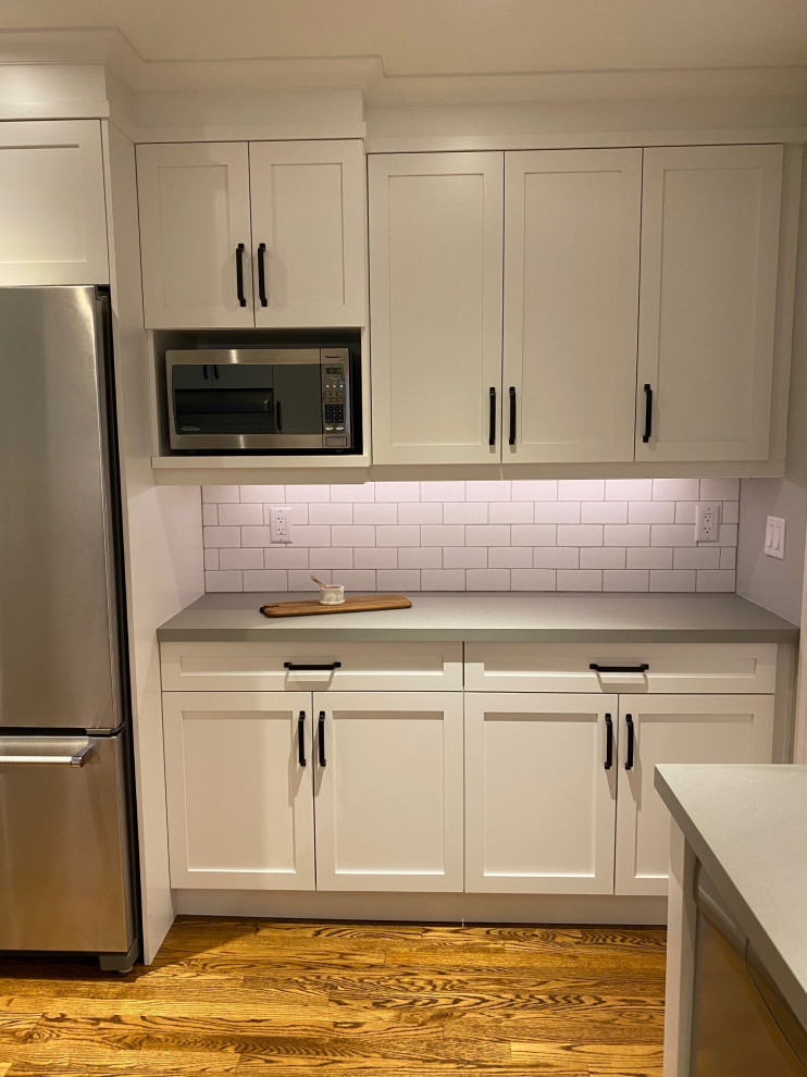 Mid-sized transitional u-shaped medium tone wood floor and brown floor open concept kitchen photo in Toronto with an undermount sink, shaker cabinets, white cabinets, quartz countertops, white backsplash, porcelain backsplash, stainless steel appliances, a peninsula and gray countertops