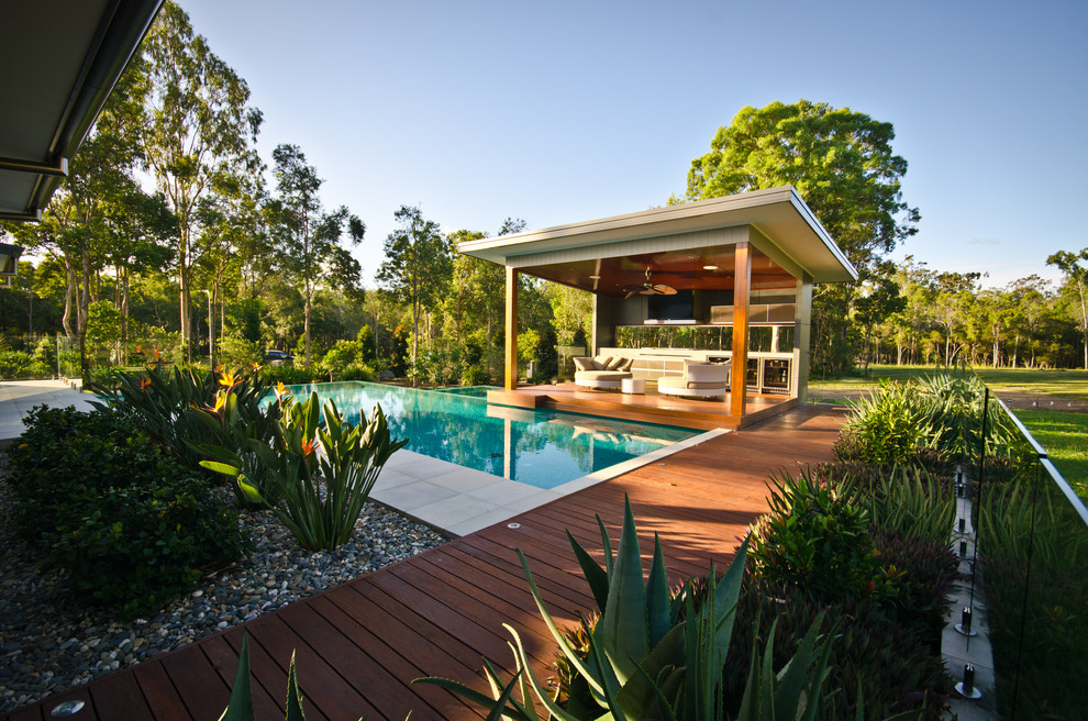 Large contemporary side yard custom-shaped infinity pool in Other with a hot tub and decking.