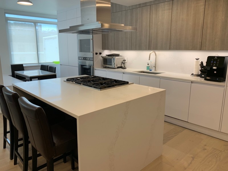 Inspiration for a large modern l-shaped eat-in kitchen in New York with an undermount sink, flat-panel cabinets, white cabinets, quartz benchtops, white splashback, stone slab splashback, stainless steel appliances, light hardwood floors, with island, multi-coloured floor and white benchtop.