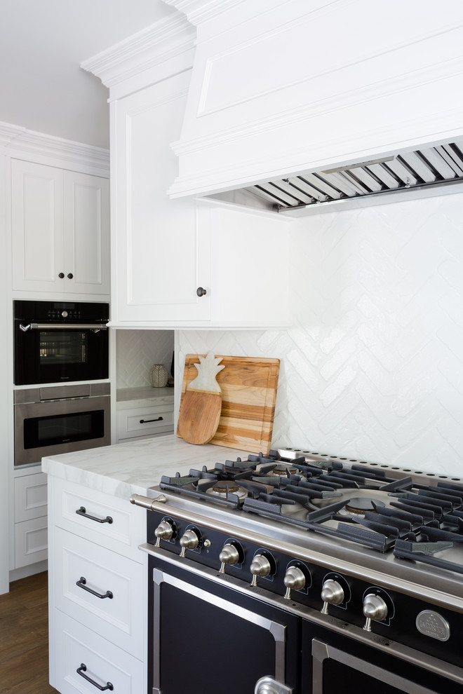 Large transitional l-shaped light wood floor open concept kitchen photo in Orange County with a farmhouse sink, shaker cabinets, white cabinets, marble countertops, white backsplash, brick backsplash, stainless steel appliances and an island