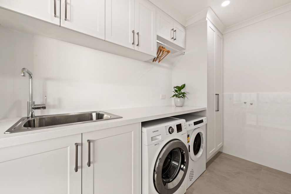 Design ideas for a mid-sized traditional single-wall laundry room in Perth with a drop-in sink, recessed-panel cabinets, white cabinets, soapstone benchtops, white walls, a side-by-side washer and dryer, beige floor and white benchtop.