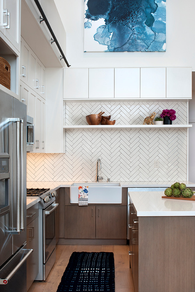 This is an example of a small scandinavian l-shaped open plan kitchen in San Francisco with a farmhouse sink, white cabinets, quartz benchtops, white splashback, subway tile splashback, stainless steel appliances, light hardwood floors, with island and flat-panel cabinets.