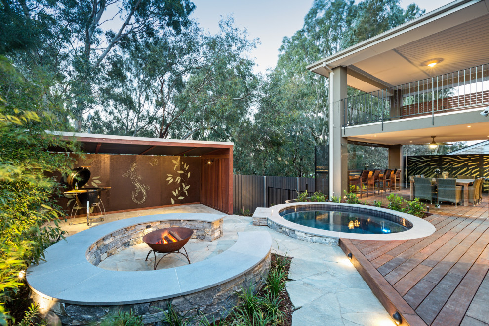 Large contemporary backyard patio in Melbourne with a fire feature and natural stone pavers.