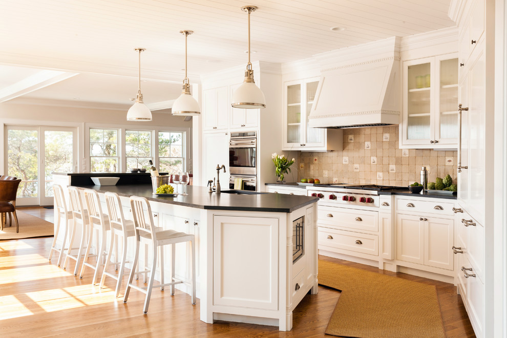 Design ideas for a traditional open plan kitchen in Boston with an undermount sink, glass-front cabinets, beige splashback, stainless steel appliances, light hardwood floors and with island.