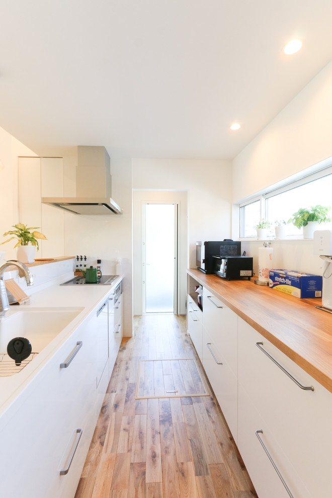 Small contemporary single-wall open plan kitchen in Other with an integrated sink, flat-panel cabinets, white cabinets, solid surface benchtops, white splashback, black appliances, medium hardwood floors, a peninsula, brown floor and brown benchtop.