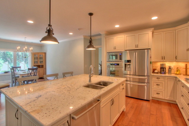 Mid-sized beach style kitchen in Atlanta with a double-bowl sink, white cabinets, granite benchtops, stone tile splashback, stainless steel appliances, medium hardwood floors and with island.